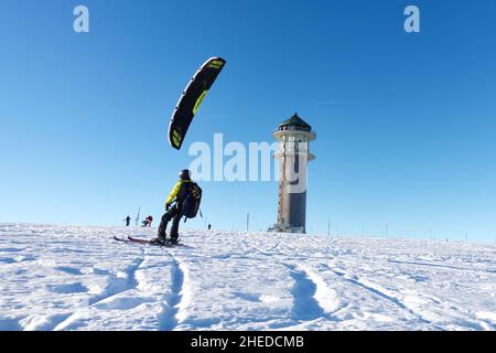 Feldberg, Deutschland - 19. Dezember 2021: 1 Wintersportler im Schnee. Schneekiter mit Rucksack auf Skiern vor blauem Himmel. Feldbergturm auf einem sonnigen ww Stockfoto