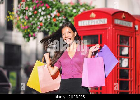 London Shopping glückliche asiatische Frau zu Fuß auf der Oxford Street, London City, mit mehreren Geschenktüten aus dem Geschäft Verkauf. Lächelndes Mädchen in rosa für den Frühling Stockfoto