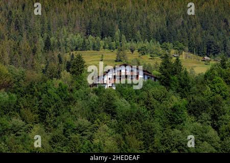 Holzhäuser in den Bergen inmitten des Waldes, am Hang, Wolken und blauer Himmel. Karpaten Stockfoto