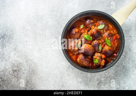 Fleischbällchen in Tomatensauce und Basilikum auf einem Tisch aus hellem Stein. Stockfoto