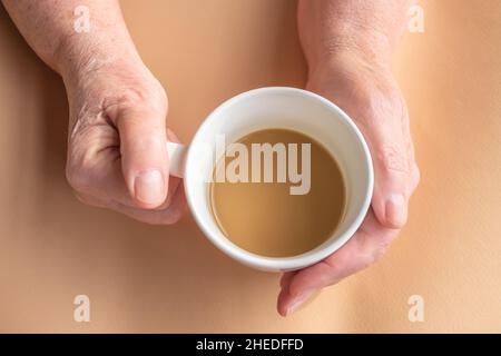 Ältere Frau hält Morgenkaffee mit Milch in der Hand Stockfoto
