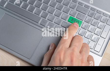 Laptop und umweltfreundliches Technologiekonzept. Drücken Sie die grüne Taste am Computer von der Hand. Stockfoto