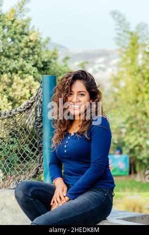 Schöne junge Frau, die auf einer Steinbank im Park sitzt Stockfoto