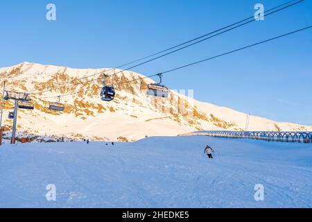 Alpe d'Huez, Frankreich - 30.12.2021 : Skiliftseilbahn am Abend auf alpinem Bergwintergebiet. Ski Sessellift Seilbahn mit Menschen. Typisch fren Stockfoto