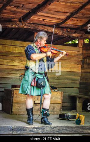 05-2016 Muskogee USA Mann im grünen Kilt mit Zöpfen und Taschen spielt Geige auf rustikaler Holzbühne - Motion Blur Stockfoto