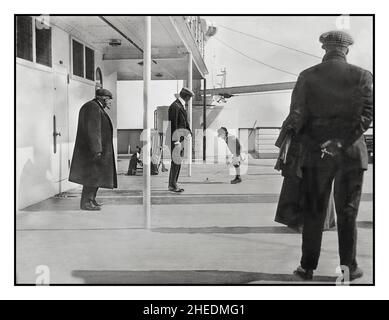 Die Passagiere von RMS Titanic auf der Achterpromenade des A-Decks: Der sechsjährige Robert Douglas Speden wirft unter den wachsamen Augen seines Vaters Frederick einen Kreisel. 11th. April 1912 3 Tage bevor die Titanic nach einem Eisberg auf tragische Weise sank, ist dieses Foto, das zu Beginn der Jungfernfahrt der Titanic aufgenommen wurde, zu sehen, wie der Passagier Douglas Spedden mit seinem Oberteil auf dem Promenadendeck des Schiffes spielt. Für alle, an die sich der sechsjährige Douglas Spedden erinnert hätte, ging er friedlich in seinem erstklassigen Kajütenzimmer auf der RMS Titanic schlafen und wachte dann bei Sonnenaufgang in einem neun Meter langen Rettungsboot auf. Stockfoto