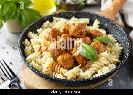 Italienische Küche. Italienische Fusilli-Pasta mit Fleischbällchen in Tomatensauce und Basilikum auf grauem Steingrund. Stockfoto