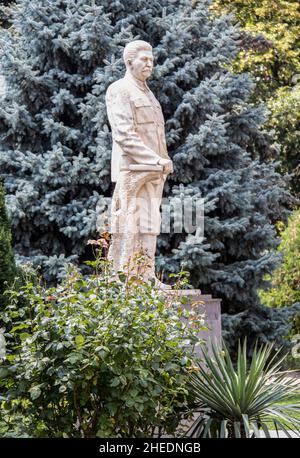 7-20 2019 Gori Georgia Stalinstatue, die mit der Hand auf einem Buch im Freien steht, umgeben von Bäumen im Park außerhalb des Stalin-Museums-Selective Focus Stockfoto