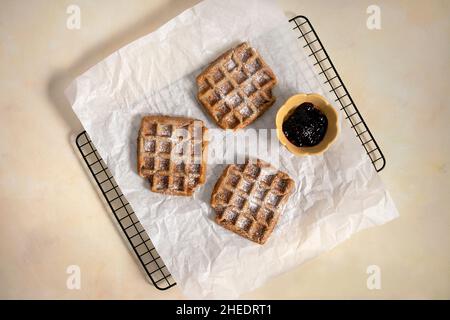 Frisch gebackene Waffeln von oben. Draufsicht auf vegane, glutenfreie Waffeln mit Marmelade und Puderzucker auf gelbem Hintergrund. Leckeres hausgemachtes Dessert. Stockfoto