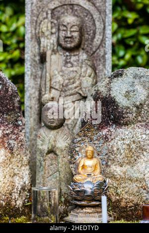 Kleine buddha-Statue mit Münzopfern zu Füßen, dahinter zwei größere Jizo-Statuen, beide außer Fokus, im Saisho-in Garden, Nanzen Tempel. Kyoto Stockfoto