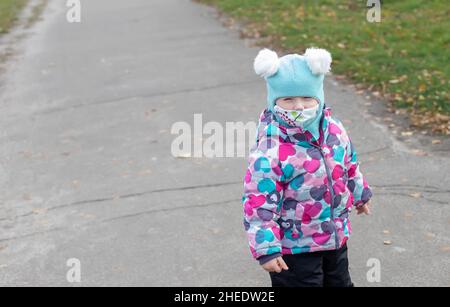 Kleines Mädchen im Winter Overalls chirurgische Verband. Coronavirus, Krankheit, Infektion, Quarantäne, medizinische Maske, COVID-19. Junge in einer medizinischen Maske. Quarantäne Stockfoto