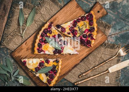 Stücke einer Preiselbeerziegenkäse-Tarte mit Salbei auf rustikalem Hintergrund, Draufsicht Stockfoto