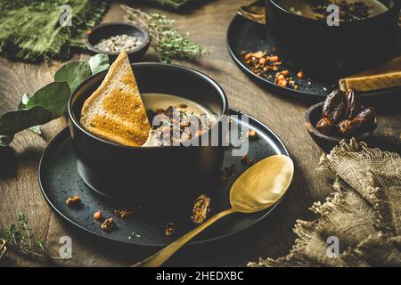 Kastaniensuppe mit rotiertem Belag, Creme und Brot in einer schwarzen Schüssel auf rustikalem Holzhintergrund Stockfoto