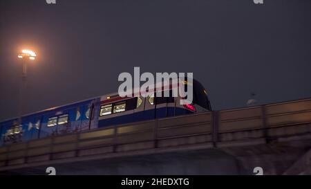 Stadtlandschaft im Hintergrund, U-Bahn nähert sich dem Bahnhof auf der rechten Seite, bewegt sich über Brücke in der Dämmerung Zeit. Video. Surface U-Bahn-Station Stockfoto