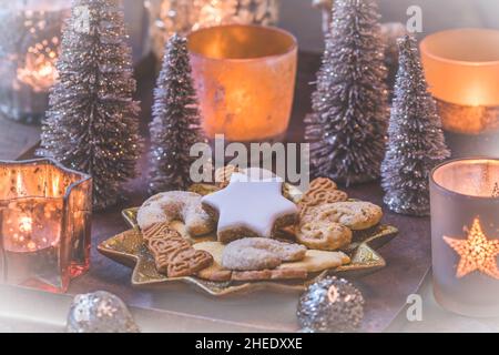 Weihnachtskekse auf einem sternförmigen Teller mit weihnachtsdekoration und Kerzenlicht Stockfoto