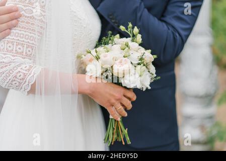 Die Braut hält in ihren Händen einen schönen Strauß aus zarten Blumen und grünen Blättern. Das Brautpaar umarmt, die Hände der Braut und des Bräutigams Stockfoto