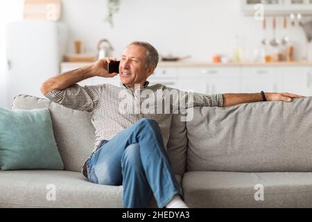 Zufriedener Reifer Mann, Der Auf Dem Handy Spricht Und Zu Hause Beiseite Schaut Stockfoto