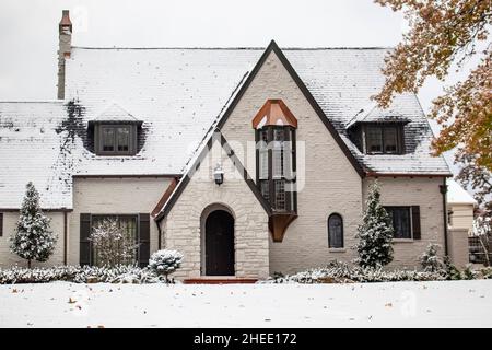 Charmantes weiß bemaltes Ziegelhaus mit Kupferakzenten bei Schneefall mit Herbstblättern noch auf Bäumen Stockfoto