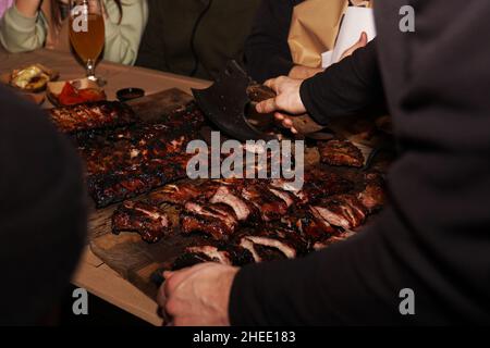 Der Kellner zerkleinert saftige Grillrippchen, wenn er den Restaurantkunden serviert. Fleisch-Restaurant in Lviv Stockfoto