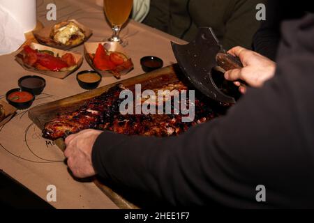 Der Kellner zerkleinert saftige Grillrippchen, wenn er den Restaurantkunden serviert. Fleisch-Restaurant in Lviv Stockfoto