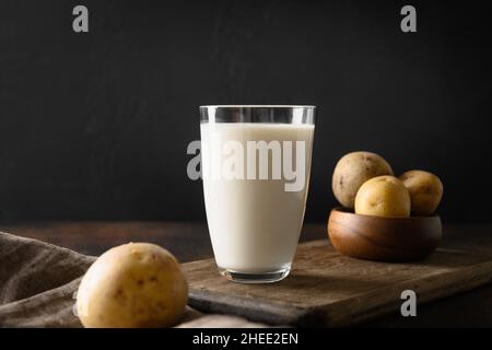 Vegane Kartoffelmilch und Kartoffel auf braunem Hintergrund. Nahaufnahme. Milchaustauschstoff auf pflanzlicher Basis und laktosefrei. Stockfoto