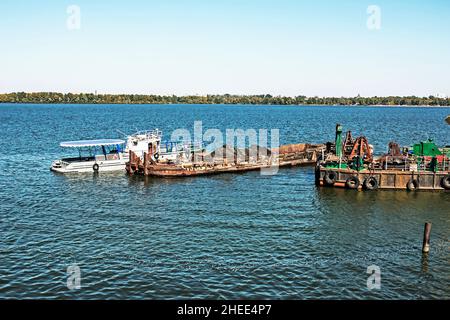 Reinigung der neu entstandenen Insel von Industrieabfällen auf dem Dnjepr mit einem Bagger. Ein Lastkahn mit einem Schlepper nimmt Müll heraus. Ökologisches Konzept. Stockfoto