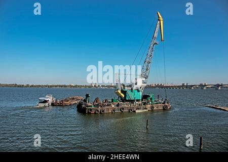 Reinigung der neu entstandenen Insel von Industrieabfällen auf dem Dnjepr mit einem Bagger. Ein Lastkahn mit einem Schlepper nimmt Müll heraus. Ökologisches Konzept. Stockfoto