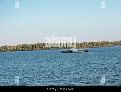 Reinigung der neu entstandenen Insel von Industrieabfällen auf dem Dnjepr mit einem Bagger. Ein Lastkahn mit einem Schlepper nimmt Müll heraus. Ökologisches Konzept. Stockfoto