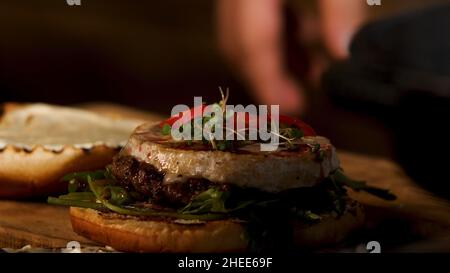 Köstliche saftige rote Chili-Pfeffer-Burger mit Rindfleisch-Cutlet und Camembert-Käse, foodporn. Nahaufnahme der männlichen Hand, die rote Kreise mit Chilischote setzt Stockfoto