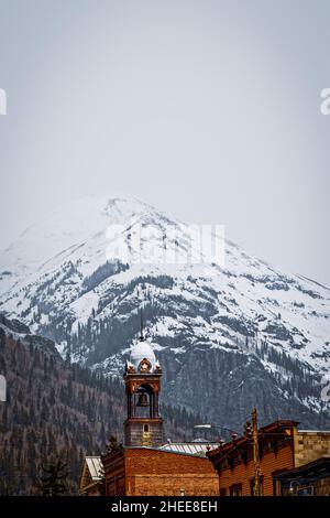 Turm des historischen alten Rathauses in Silverton Colorado in den San Juan Mountains in Colorado CA USA mit schneebedeckten Bergen im Hintergrund auf bewölktem Untergrund Stockfoto