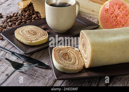 Bolo de rolo Scheiben aus der Nähe, umgeben von Besteck, Guava, Tasse und Kaffeebohnen. Stockfoto