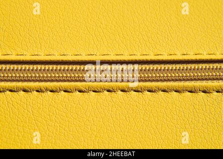 Nahaufnahme eines gelben Reissverschlusses auf Leder oder Kunstleder. Kleidung und Accessoires Hintergrund. Gerader Reißverschluss. Stockfoto