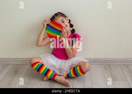 Ein fröhliches, kleines Brünette Mädchen, das einen Regenbogen hält, knallt in ihre Hände. Stockfoto