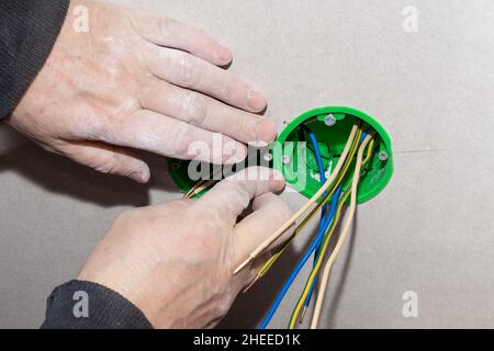 Ein Elektriker installiert eine Steckdose in die Wand. Elektrische Verdrahtung im Haus durchführen. Stockfoto