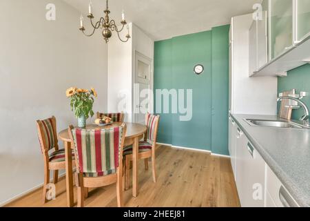 Altmodische Holzstühle und ein runder Tisch mit Blumenvasen in der modernen Küche mit weißen Möbeln bei Tageslicht Stockfoto