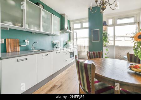 Altmodische Holzstühle und ein runder Tisch mit Blumenvasen in der modernen Küche mit weißen Möbeln bei Tageslicht Stockfoto