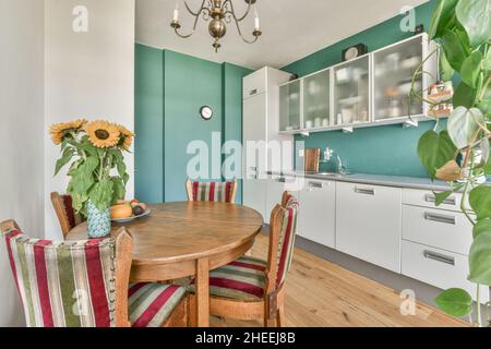 Altmodische Holzstühle und ein runder Tisch mit Blumenvasen in der modernen Küche mit weißen Möbeln bei Tageslicht Stockfoto