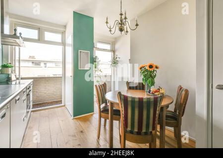 Altmodische Holzstühle und ein runder Tisch mit Blumenvasen in der modernen Küche mit weißen Möbeln bei Tageslicht Stockfoto