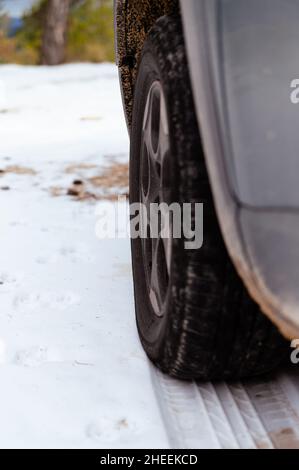 Von unten aus Nahaufnahme des Rades des geparkten Autos und der Laufspur, die am Wintertag auf verschneiten Boden gelegt wurde Stockfoto