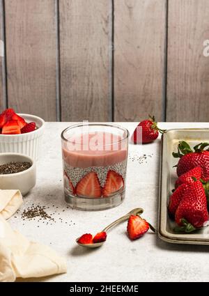 Leckerer Pudding mit Chiasamen und Scheiben frischer Erdbeeren, die in der Nähe der Zutaten für ein gesundes Frühstück auf den Tisch gelegt werden Stockfoto