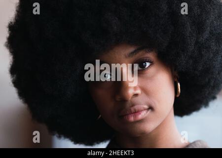 Porträt einer unemotionalen attraktiven afroamerikanischen Frau mit stilvoller schwarzer Afro-Frisur, die im hellen Raum auf die Kamera schaut Stockfoto