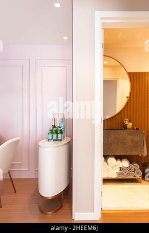 Tisch mit Flaschen Getränke und Champagner mit geöffneter Badezimmertür mit Spiegel über Waschbecken und Handtüchern Stockfoto