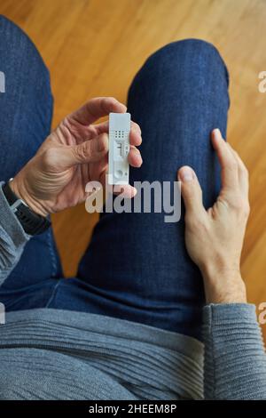 Anonyme Person in Jeans, die mit einem negativen covid Schnelltest sitzt Stockfoto