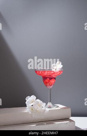 Kristallglas margarita Cocktail aus Granatapfel, serviert mit Blumenblüten auf Betonblöcken im Studio Stockfoto