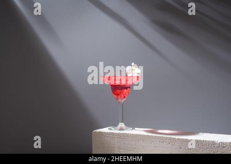 Kristallglas margarita Cocktail aus Granatapfel, serviert mit Blumenblüten auf Betonblöcken im Studio Stockfoto