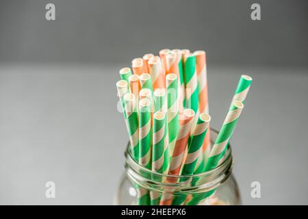 Papierhalme in einem Glas vor einem grauen Hintergrund. Stockfoto