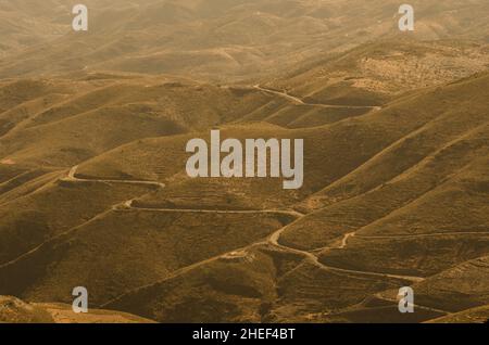 Berge, Täler und Schluchten einer Wüste, wo ein trostloser Pfad die Einöde durchquert Stockfoto