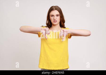 Schrecklicher Service. Porträt von unzufrieden attraktiven Teenager-Mädchen in gelben casual T-Shirt zeigt doppelte Daumen nach unten und Grimacing vor Ekel. Innenaufnahme des Studios isoliert auf grauem Hintergrund. Stockfoto