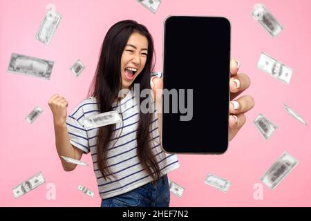 Online-Investitionen, Gewinner überglücklich reiche Frau und Geld verdienen. Porträt der staunenden jungen Frau zeigt mobile leere Display und feiert ihren Sieg. Indoor isoliert auf rosa Hintergrund. Stockfoto