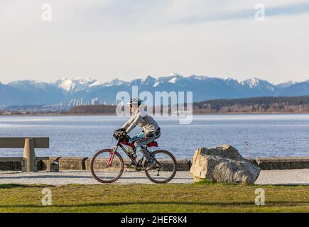 Lächelnd fit ältere Frau auf einem Fahrrad in einem Park. Glückliche ältere Frau mit Helm auf dem Sportfahrrad. Straßenfoto, Reisefoto, Konzeptfoto aktiv Stockfoto